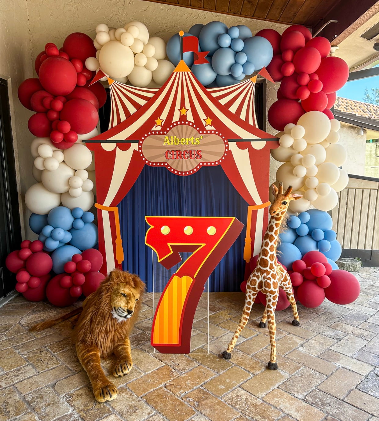 Circus-themed 7th birthday balloon arch with red, blue and cream balloons in South Florida & Miami