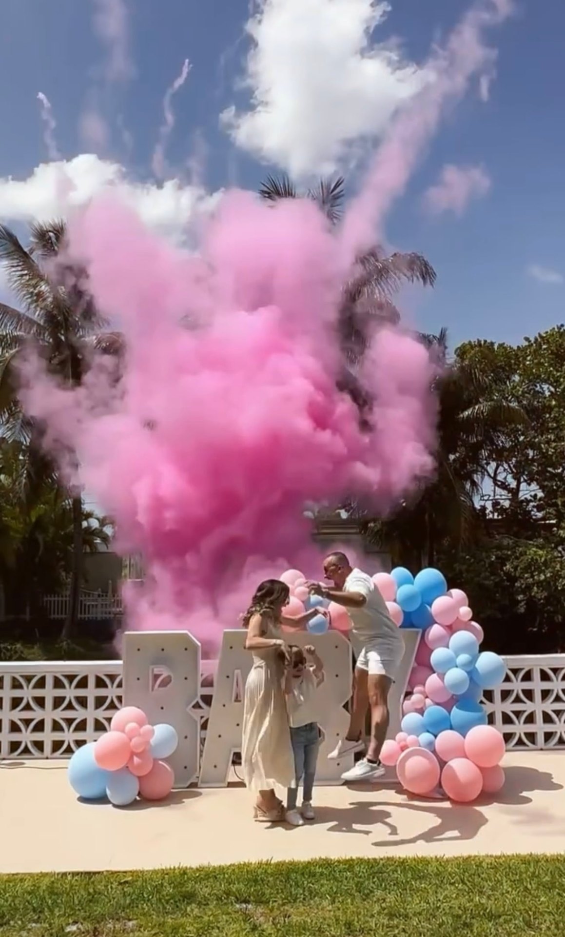 Pink gender reveal celebration with balloon clusters and smoke burst
